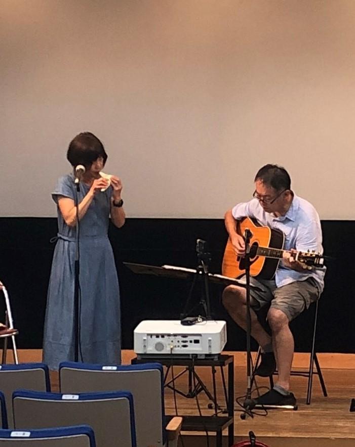 左に立ってオカリナを演奏する女性と、右で座ってギターを演奏する男性